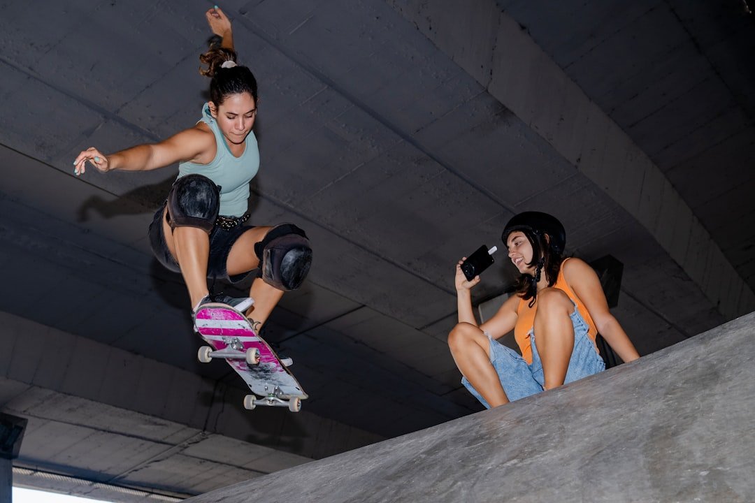 Female skateboarder in air, friend drinks on ledge