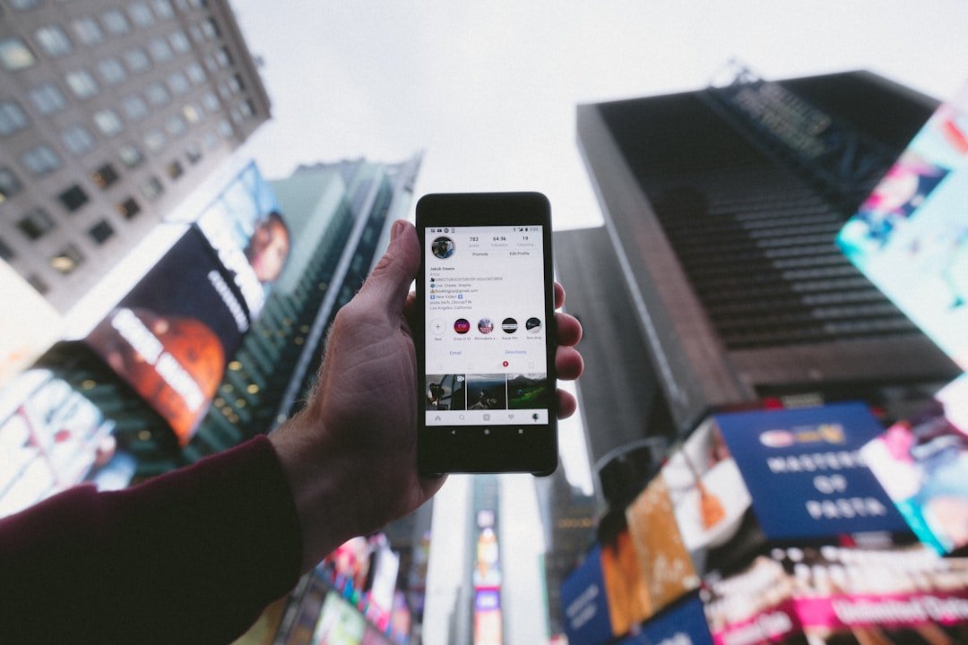 A hand holding a smartphone displaying an Instagram profile against tall city buildings